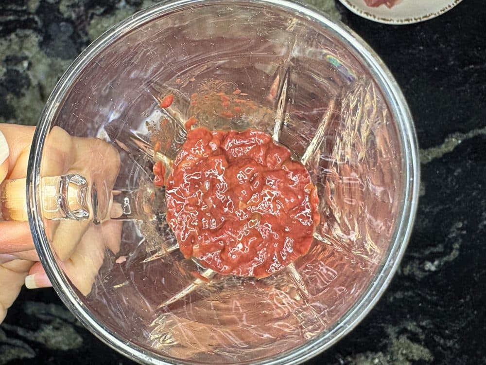 Kitchen scissors snipping raw liver into a small glass cup, pot blurred in background